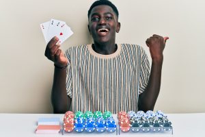 young african american man playing poker holding cards pointing thumb up side smiling happy with open mouth